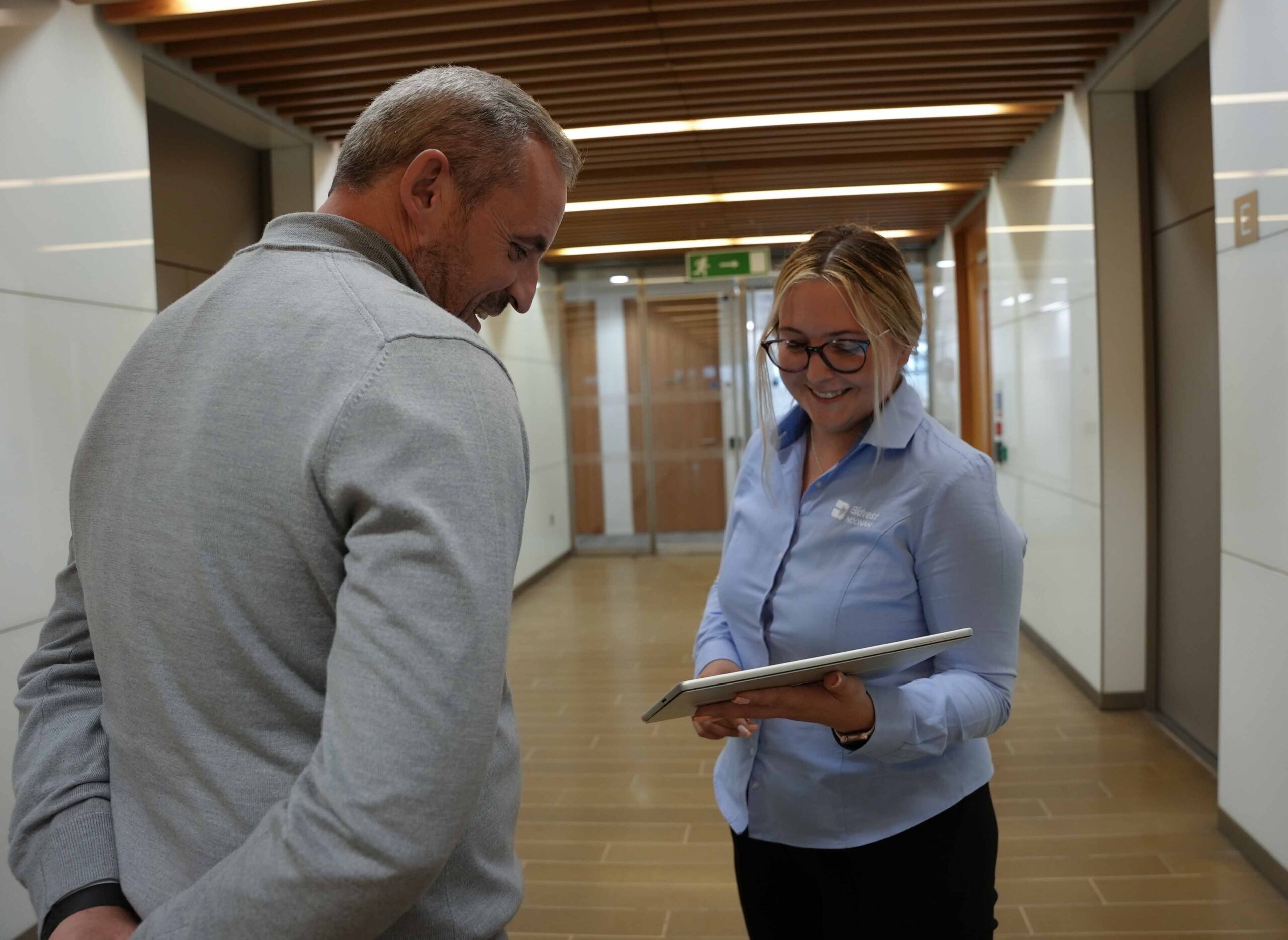 A Bidvest Noonan team member shows a client information on a tablet while discussing operations in a modern office hallway.